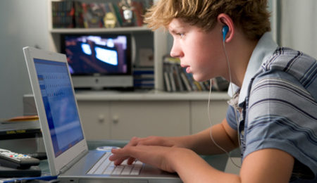 Young Boy In Bedroom Using Laptop And Listening To MP3 Player