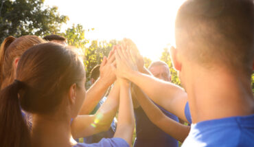 Group Of Volunteers Joining Hands Together Outdoors On Sunny Day