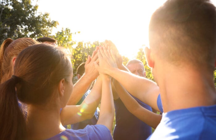 Group Of Volunteers Joining Hands Together Outdoors On Sunny Day