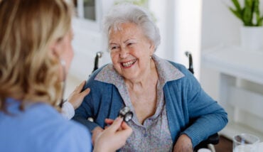 Nurse Examining Senior Patient With Stethoscope At Her Home. 